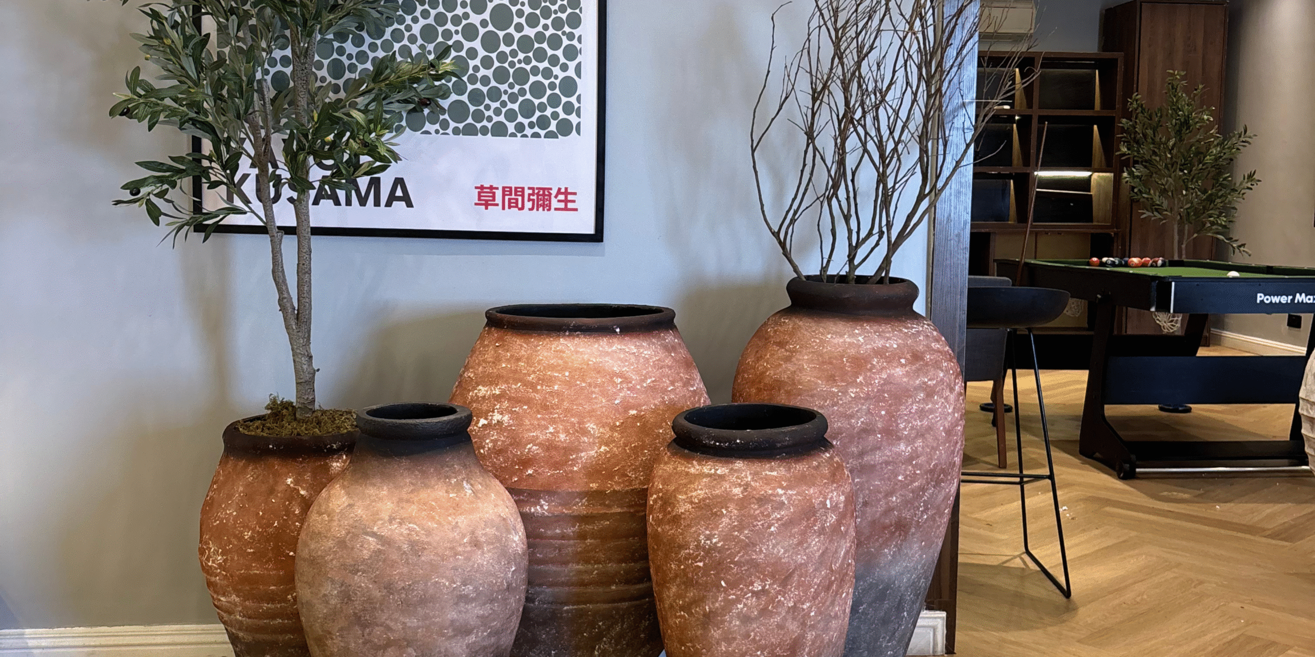 Arrangement of rustic, natural-toned terracotta planters with artificial olive trees and branches in a modern indoor space .